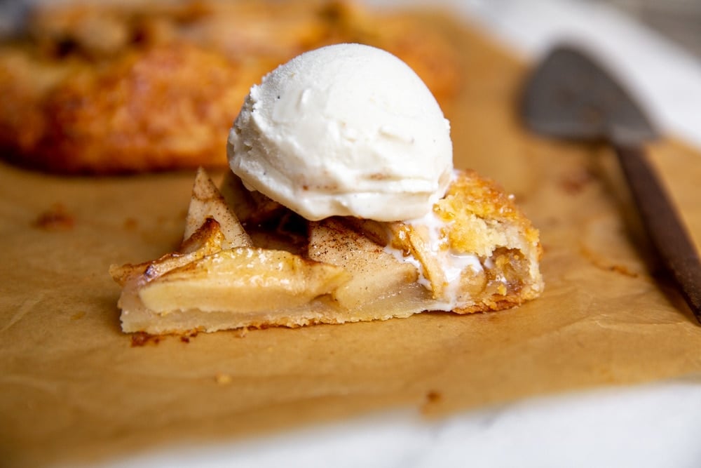 A slice of apple galette on a piece of parchment paper, topped with a scoop of vanilla ice cream. 