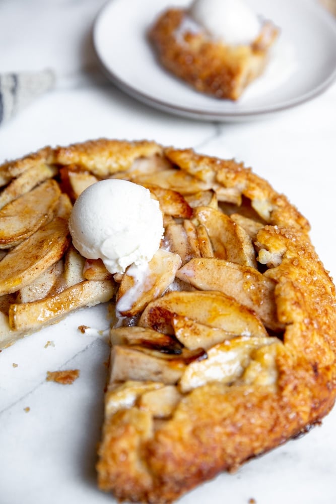 A gluten free apple galette on a marble surface topped with ice cream. 