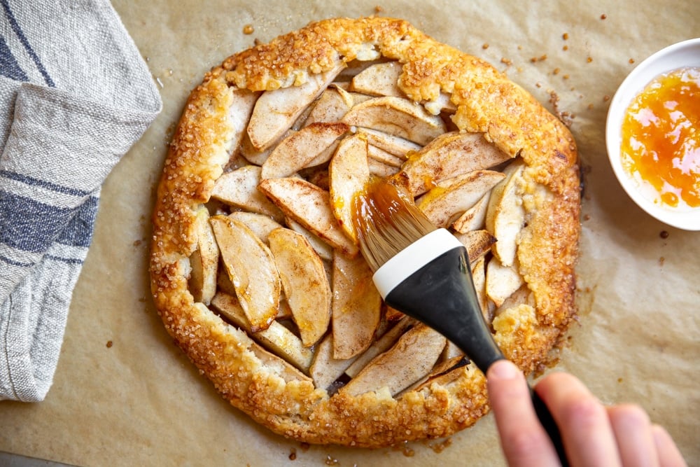 Hand brushing warm apricot jam over the apples in the baked galette. 