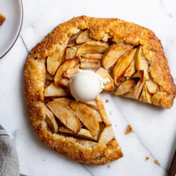 Easy apple galette on a marble surface with a slice taken out, topped with a scoop of vanilla ice cream.