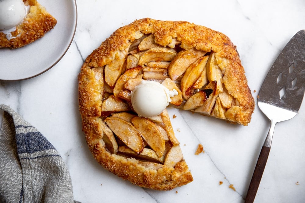 Easy apple galette on a marble surface with a slice taken out, topped with a scoop of vanilla ice cream.