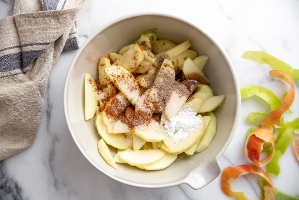 A bowl filled with the apple galette recipe filling, including sliced apples, cinnamon, cardamom, vanilla and cornstarch.  