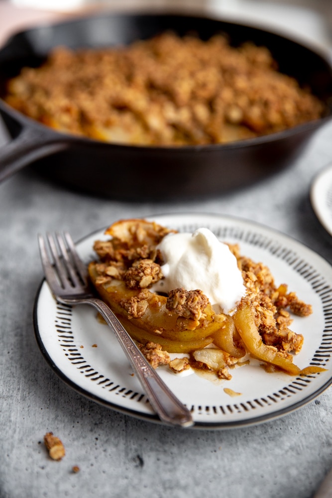 A serving of pear crisp on a plate, topped with whipped cream. 