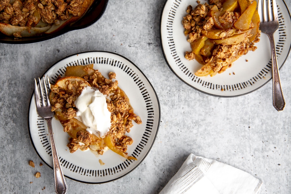 Two dessert plates topped with pear crumble, one with whipped cream. 