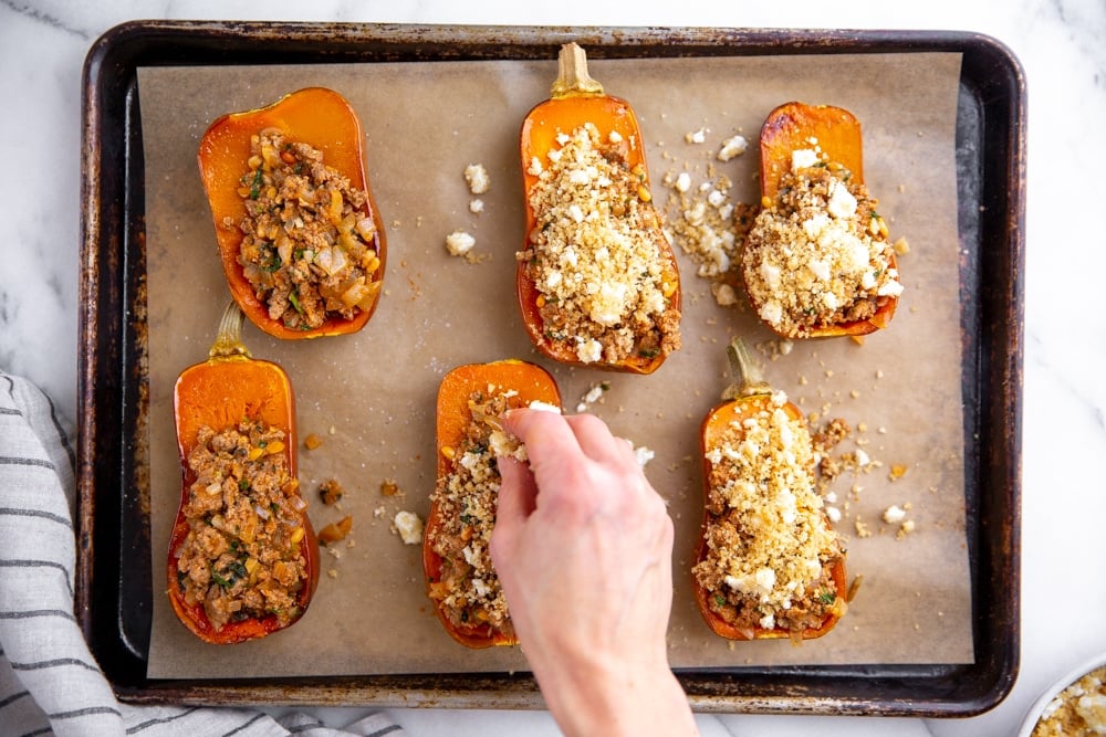 Hand sprinkling the breadcrumb topping over the stuffed squash. 