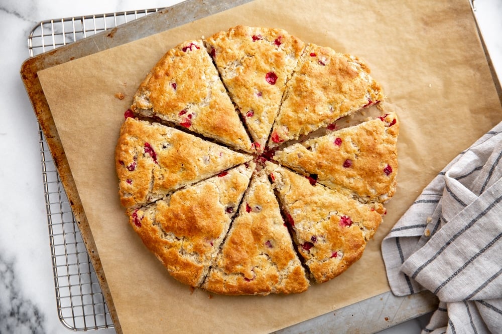 The baked cranberry scones on a baking sheet, cooling on a rack.