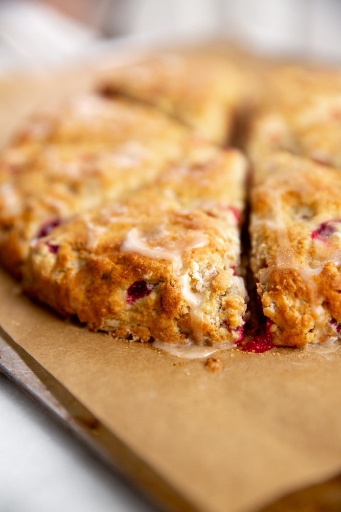 Close up of the a cranberry scone with orange glaze on a parchment lined baking sheet. 