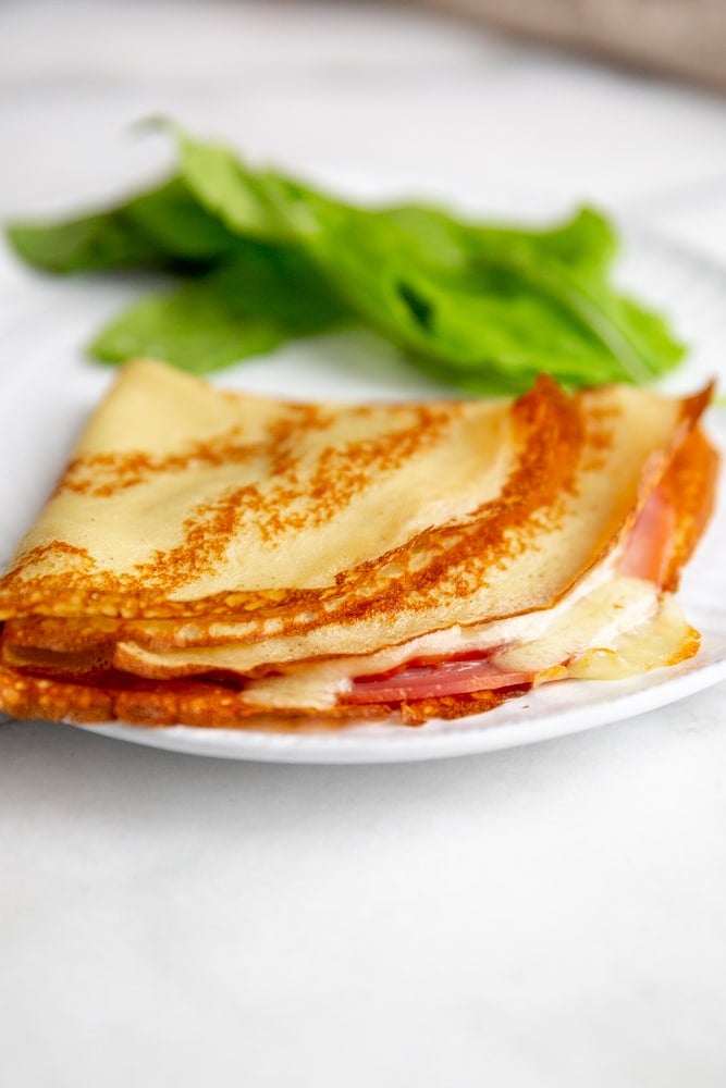 Gluten free ham and cheese crepe on a plate with a green salad.