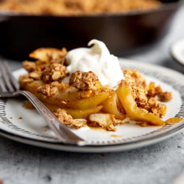 Gluten free pear crumble on a plate topped with whipped cream.