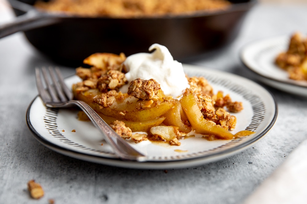 Gluten free pear crumble on a plate topped with whipped cream.