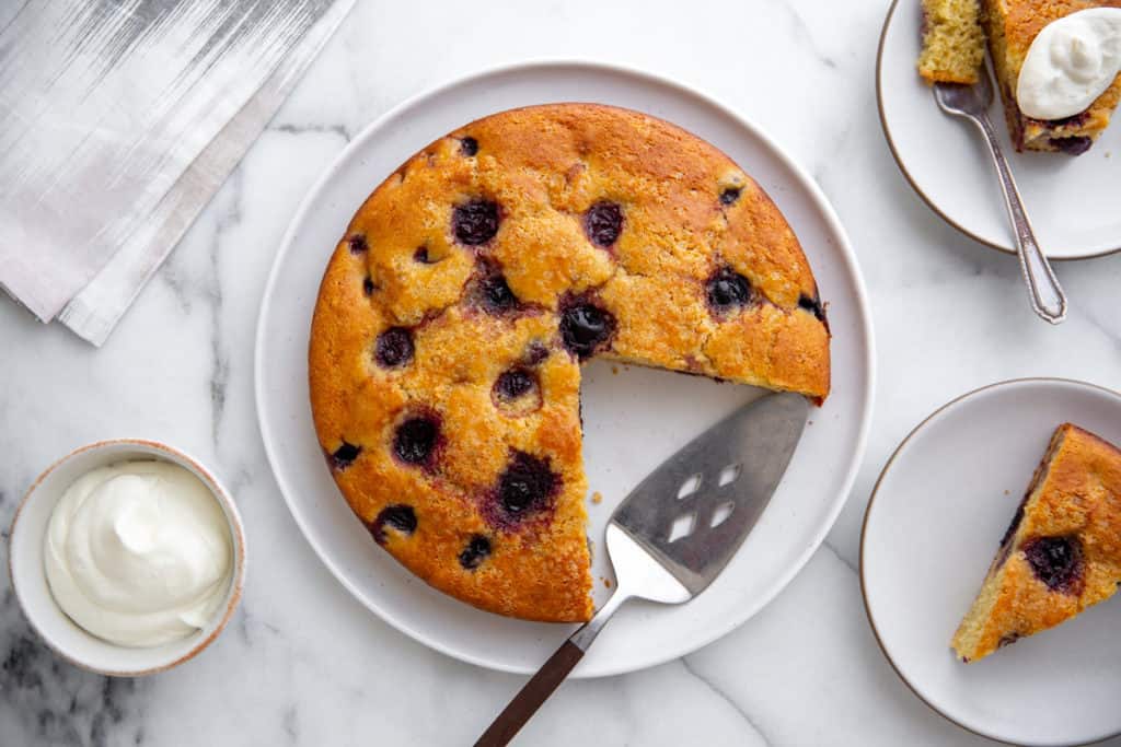 Cherry ricotta cake on a platter with whipped cream alongside.