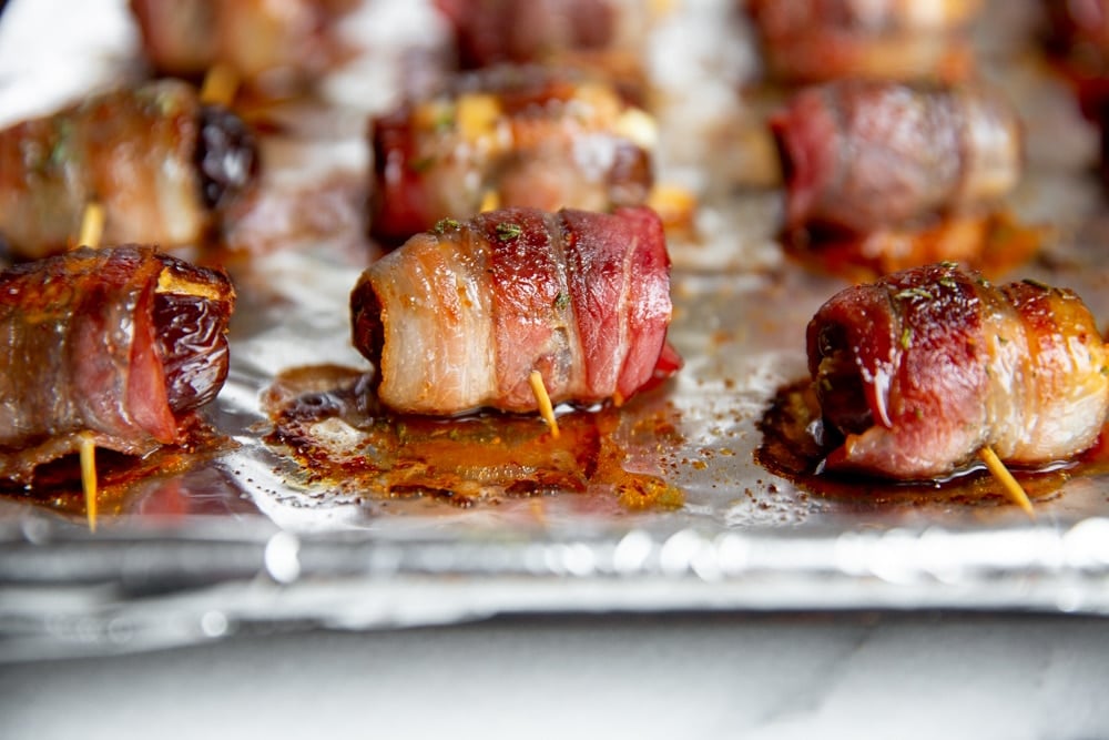 Cooked bacon wrapped dates on a baking sheet. 