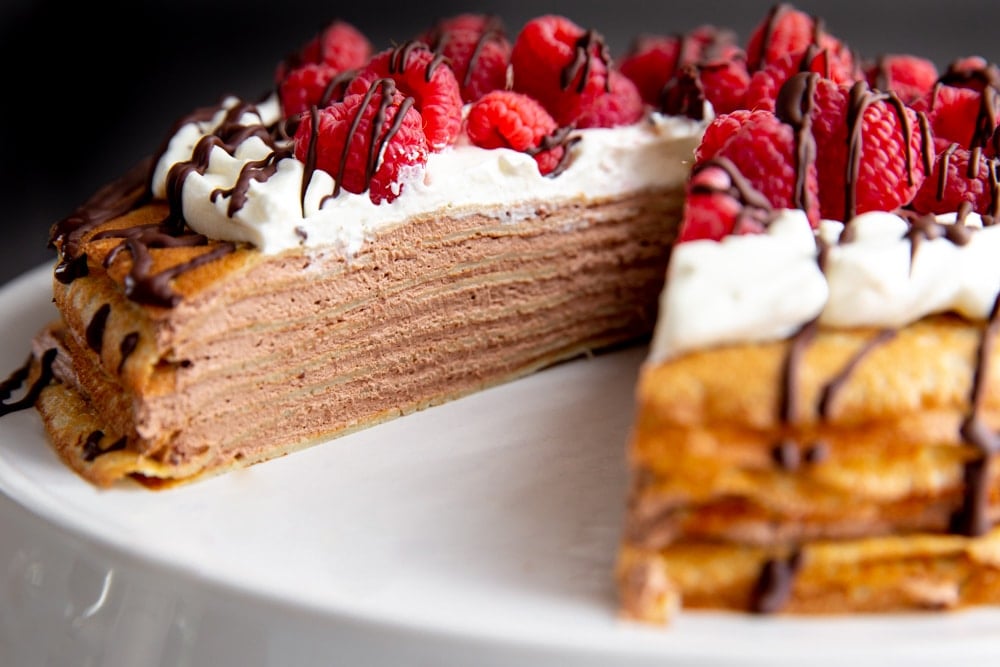 Crepe cake on a platter with a slice removed.