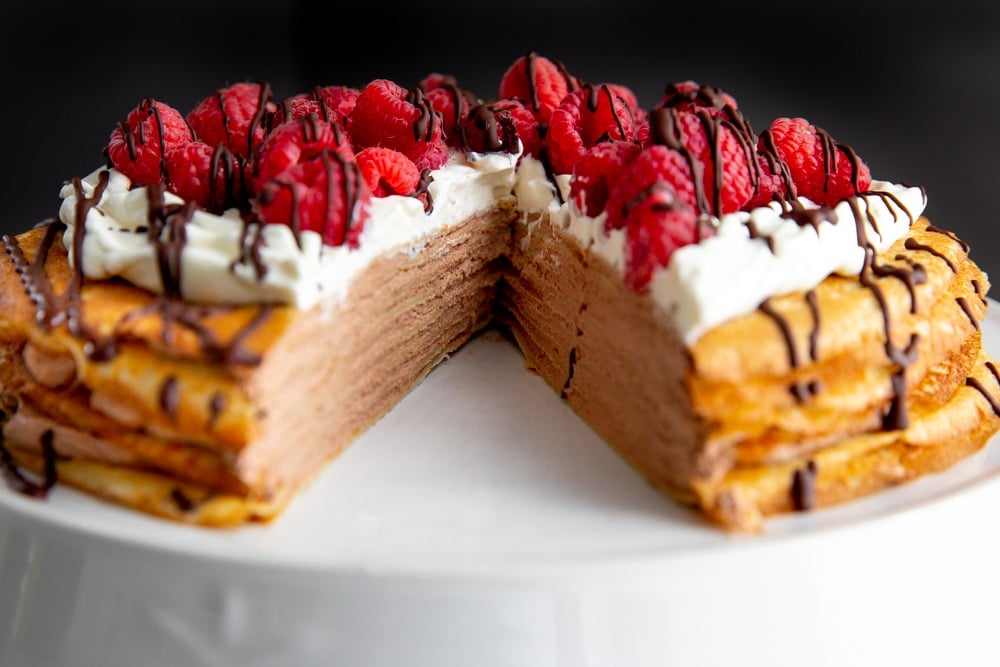 Crepe cake on a cake stand with a slice cut out.