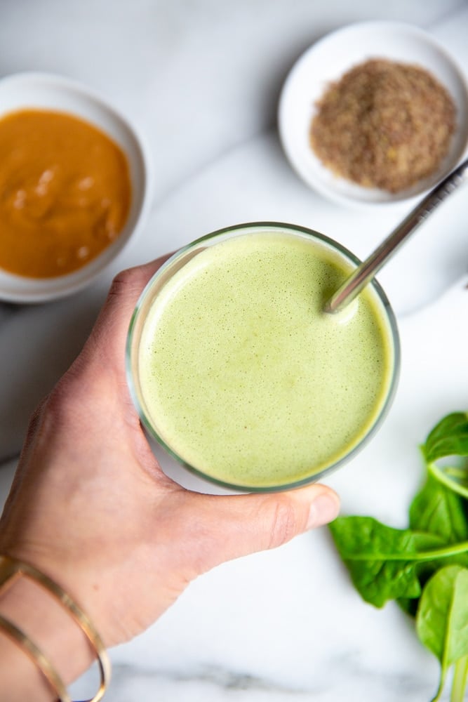 Hand holding a green smoothie in a glass with a metal straw. 