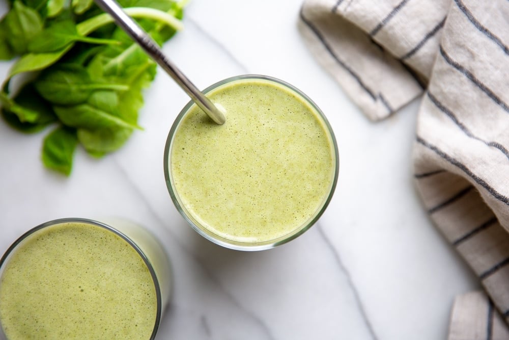 Two low sugar green smoothies in glasses on a marble surface. 