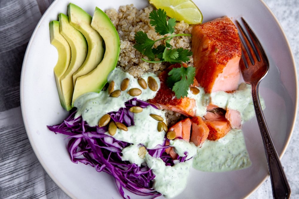 Close up of the cilantro yogurt sauce drizzled over a power bowl featuring salmon, avocado and shaved red cabbage. 