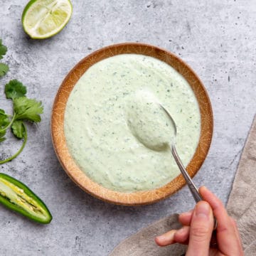 A hand holding a spoon in a bowl of cilantro yogurt sauce.
