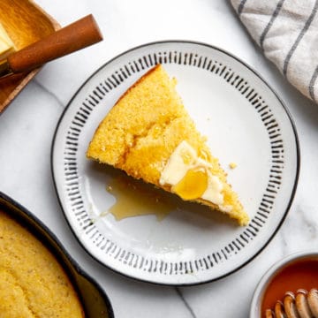 A slice of gluten free cornbread on a plate topped with butter and honey.