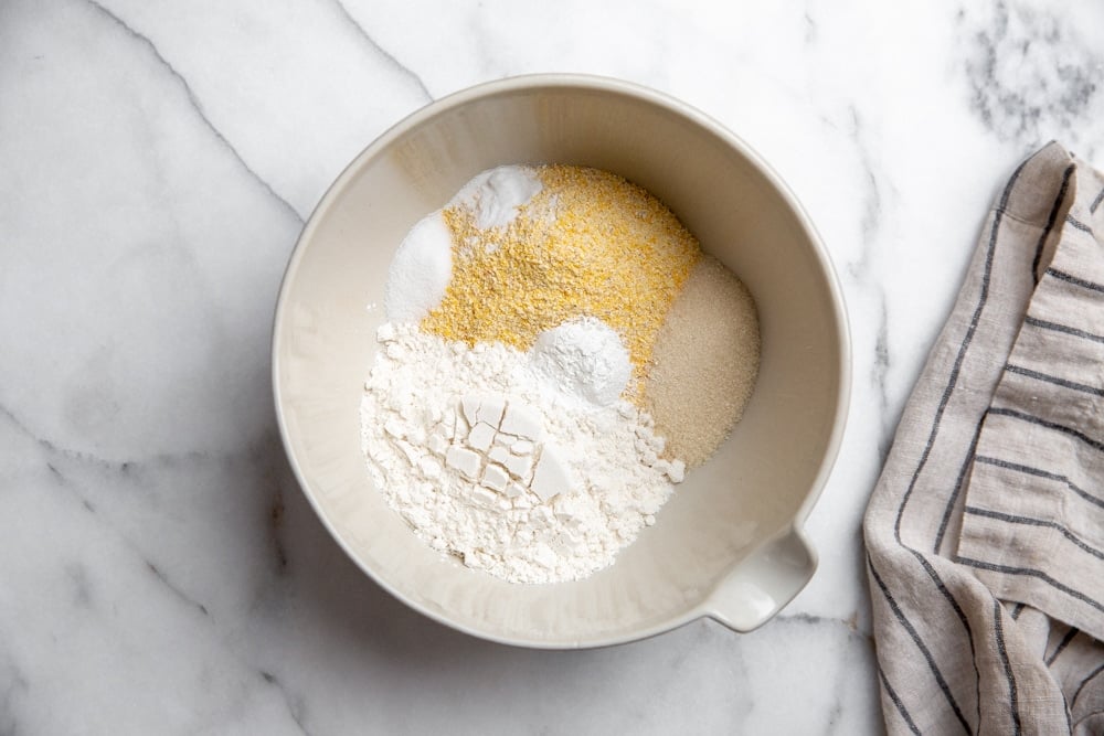 Process shot showing cornmeal, flour, sugar, baking powder, baking soda and salt in a bowl. 