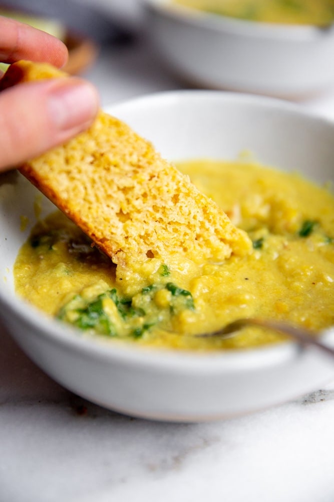 Hand dunking a piece of cornbread into the slow cooker red lentil soup. 