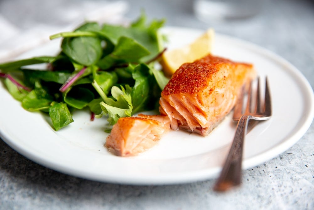A slow cooker salmon fillet on a plate with a fork, with salad greens alongside.