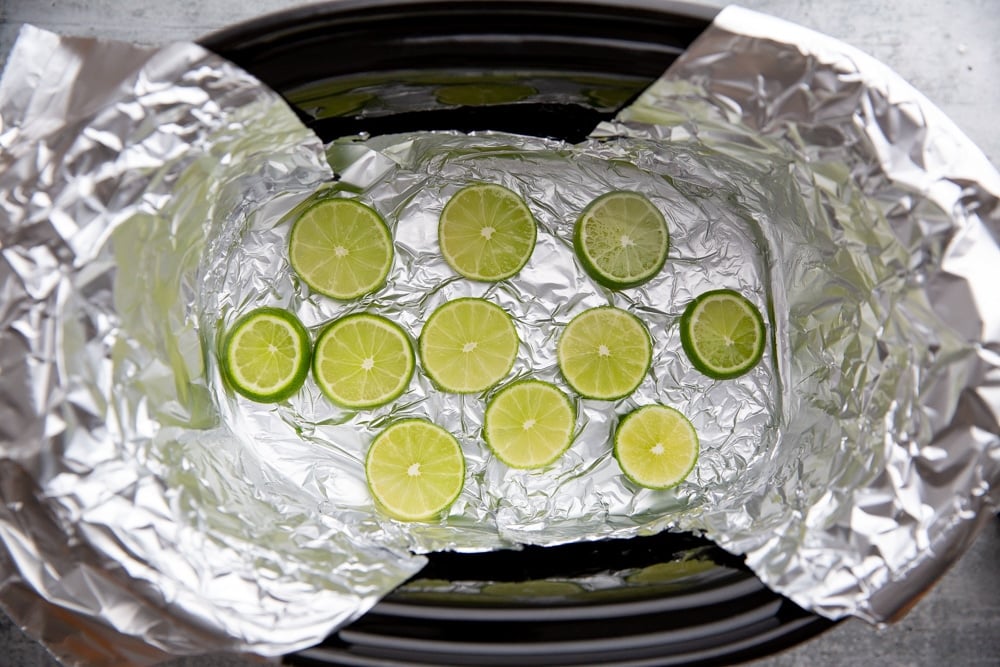 Process shot showing limes arranged on the bottom of the slow cooker. 