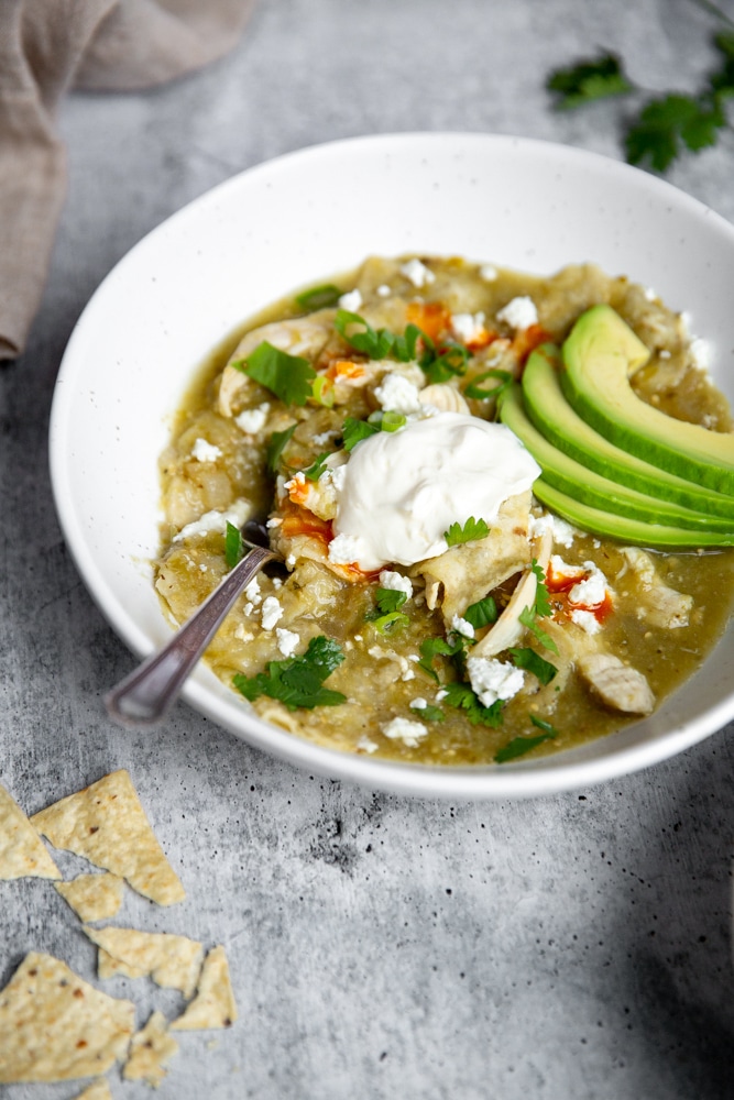 Chilaquiles chicken stew in a bowl with a spoon, topped with sour cream and avocado.