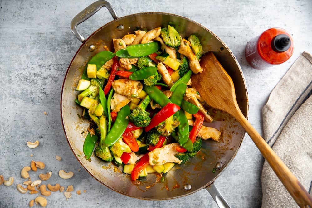 Healthy stir fry in a wok with sriracha alongside.