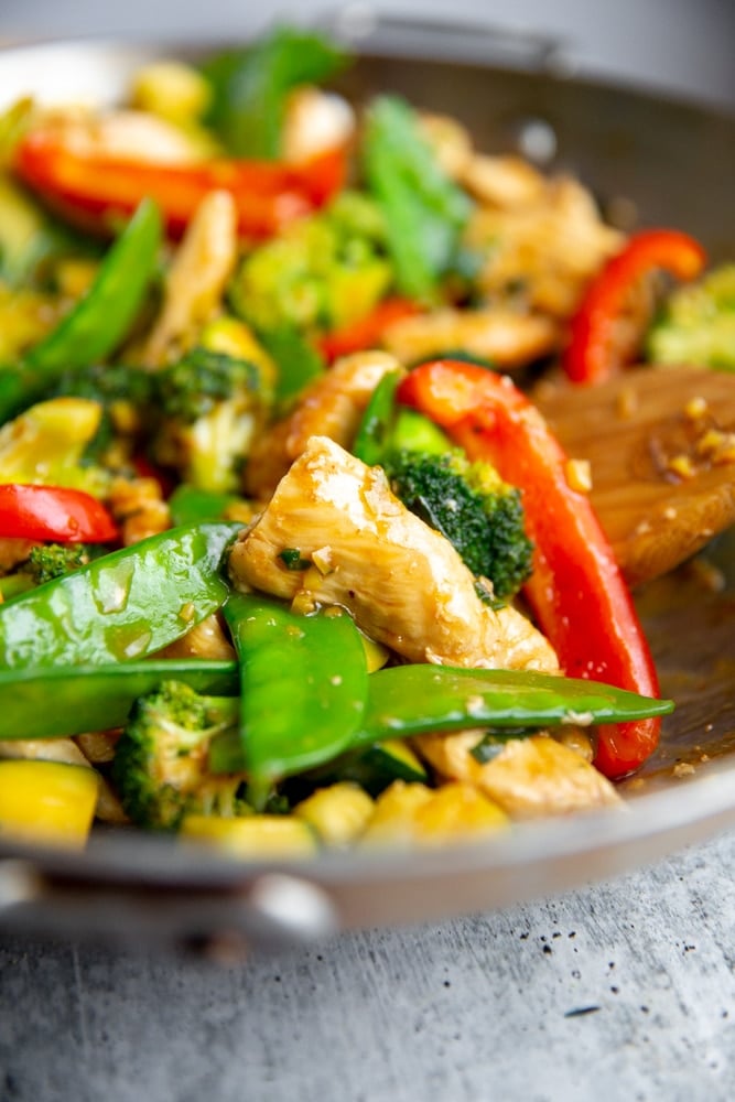 Close up of a stir fry in a wok with a wooden spoon.