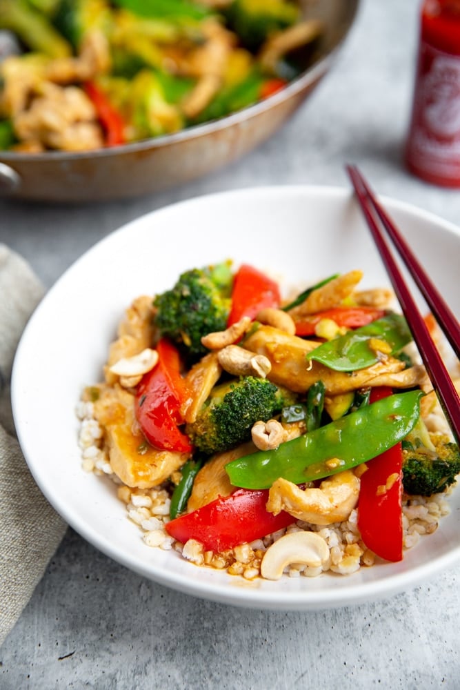 Healthy stir fry over brown rice in a bowl, with chopsticks alongside.