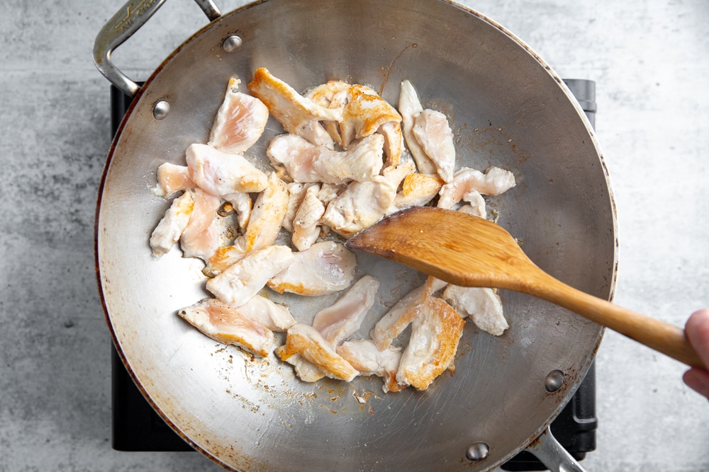 Process shot showing partially cooked chicken in a wok.