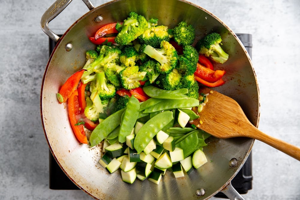 Process shot showing tender vegetables going into a healthy stir fry in a work.