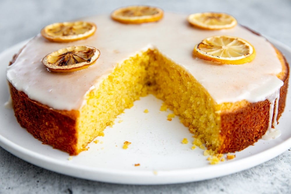 The lemon olive oil cake on a platter with a large wedge cut out.