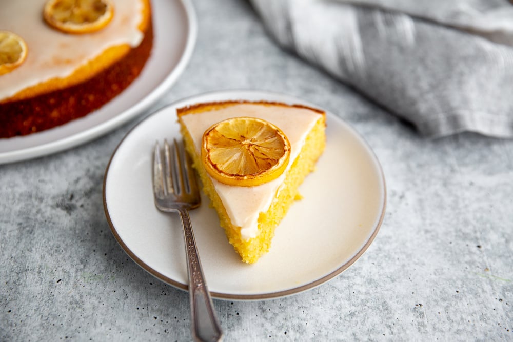 A slice of lemon olive oil cake on a plate with a fork.