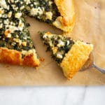 Gluten free spinach tart on a piece of parchment paper with a slice being pulled out.