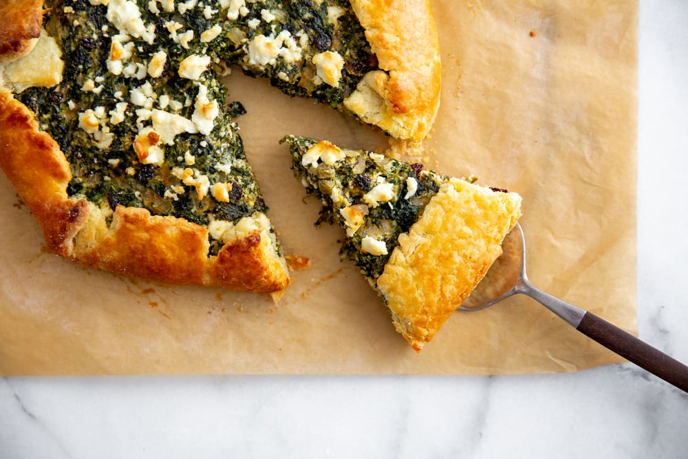 Gluten free spinach tart on a piece of parchment paper with a slice being pulled out.