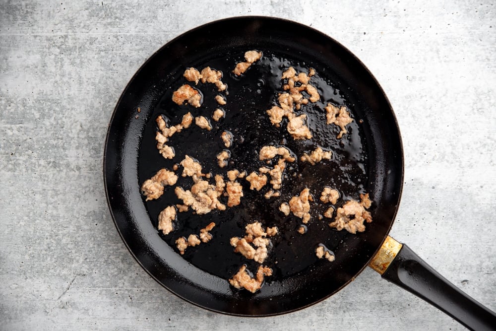 Process shot showing ground pork cooking in a non-stick skillet. 