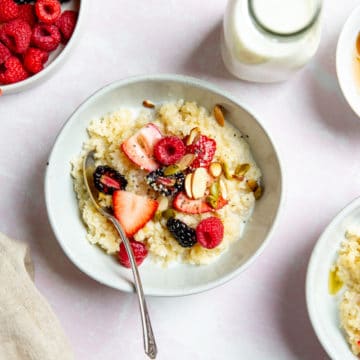 Vegan millet breakfast bowls topped with fresh fruit and nuts, with berries and milk alongside.