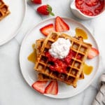 High protein strawberry oat waffles on a plate, topped with strawberries and cottage cheese.