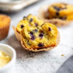 A halved blueberry cornmeal muffin, with other muffins in the background.