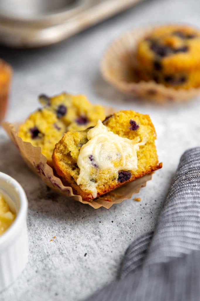 Close up of a halved blueberry cornmeal muffin, topped with softened honey butter. 