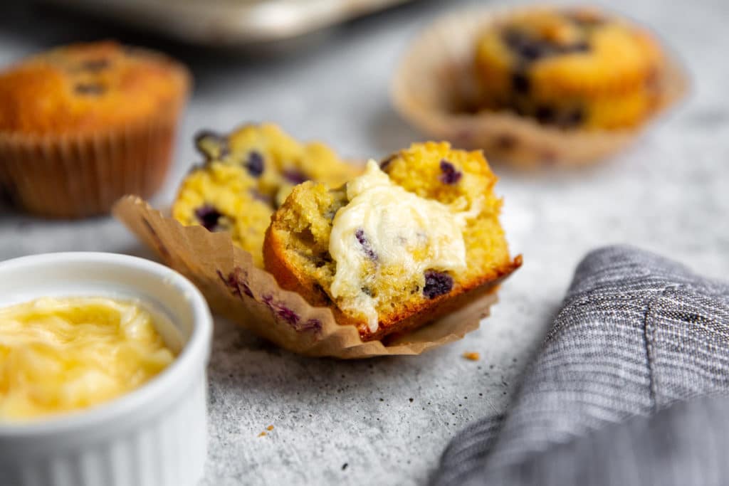 A halved gluten free blueberry corn muffin topped with softened butter.