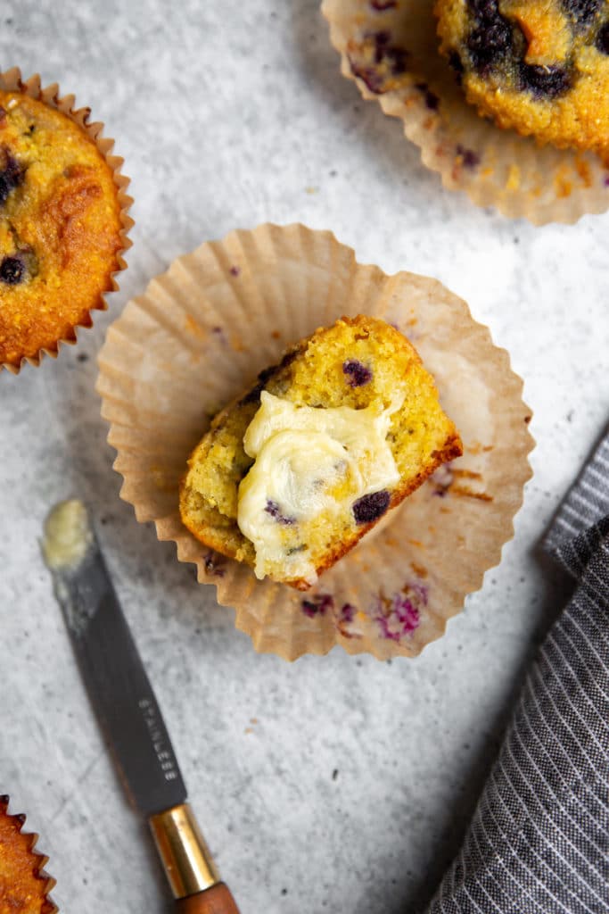 A halved blueberry cornmeal muffin topped with honey butter.