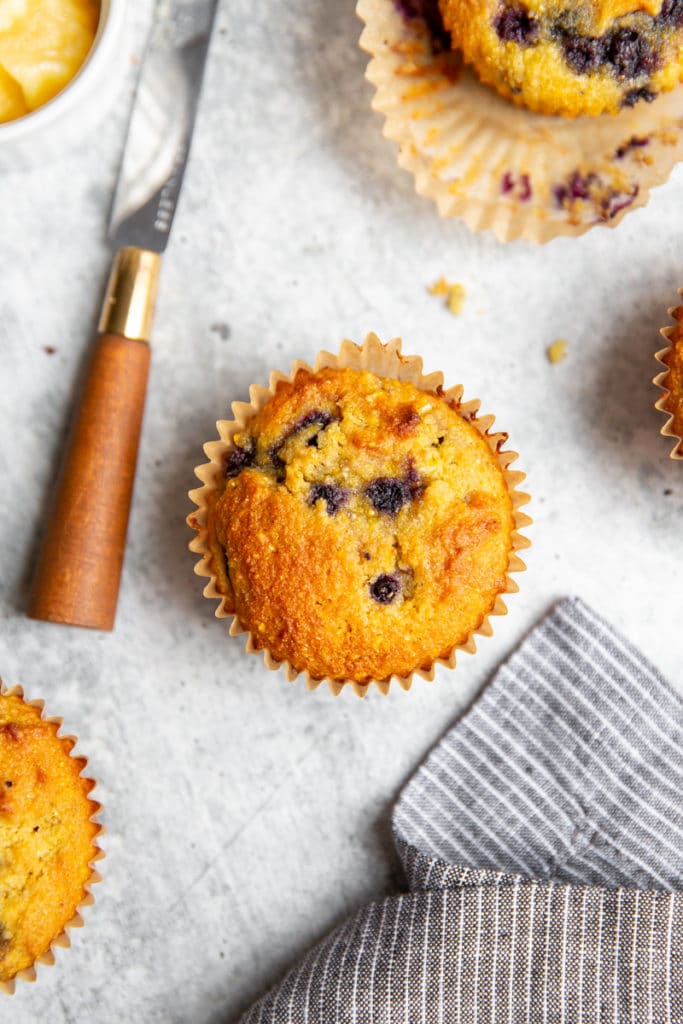 Overhead shot of a blueberry corn muffin on a countertop, with a small knife alongside.