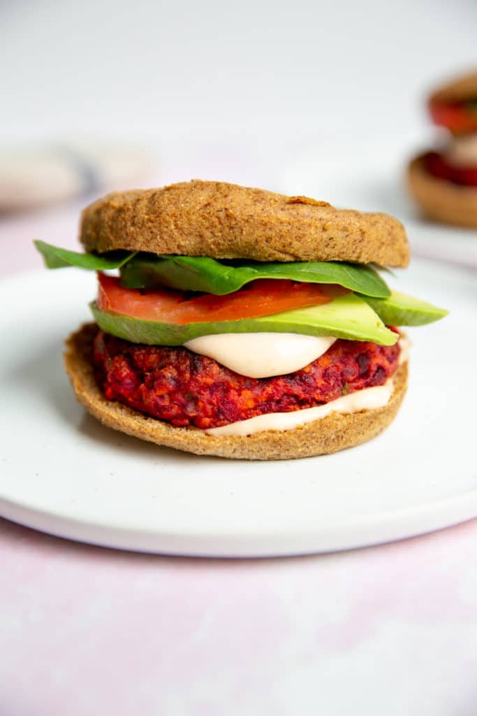 A gluten free veggie burger on a plate, topped with avocado, tomato and lettuce.