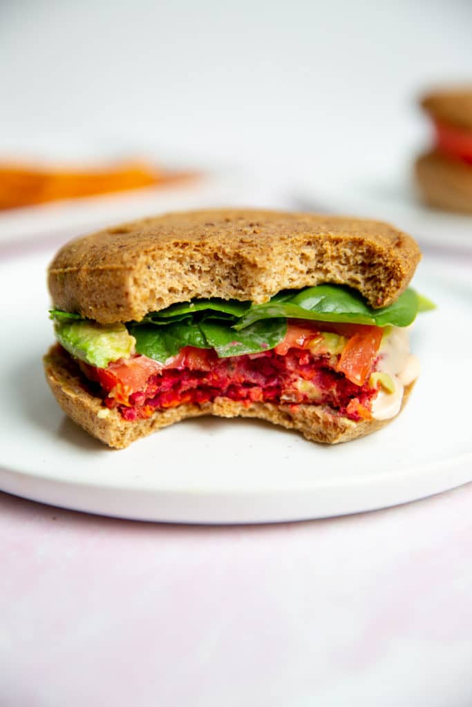 A gluten free veggie beet burger on a plate with two bites removed. 