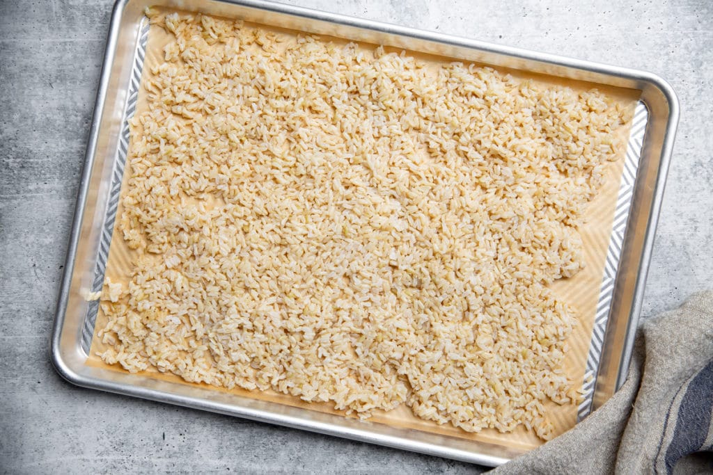 Brown rice spread out on a parchment lined baking sheet to cool.