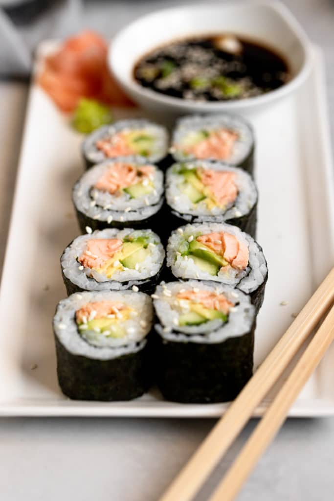 Homemade salmon avocado sushi on a plate with chopsticks.