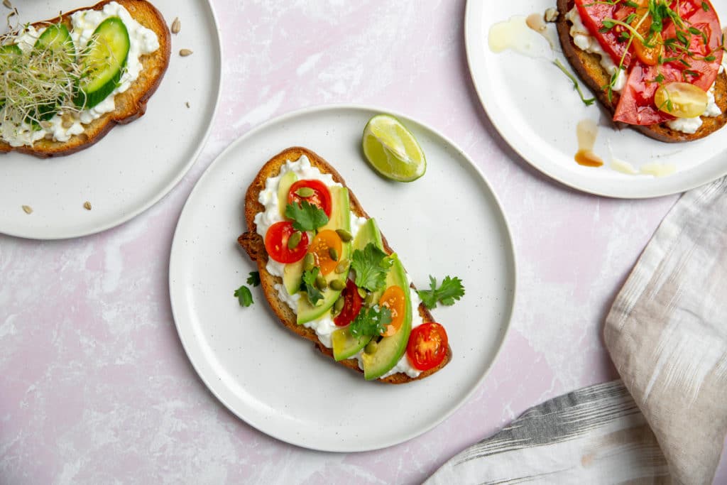 Cottage cheese toast topped with avocado and tomatoes on a plate.